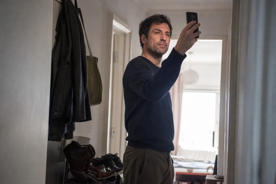 Man in his forties doing a quick selfie age check on his phone in his hallway