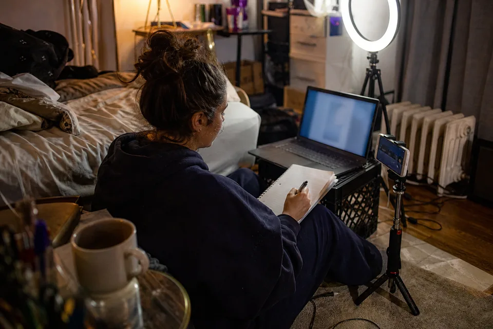 Creator on her bedroom floor writing a list of creator platforms next to her laptop and ring light