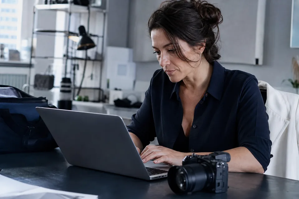 Creator editing a video on a laptop with a camera beside her