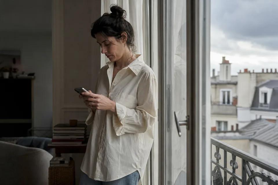 Creator typing on her phone by a tall window while the verification steps load