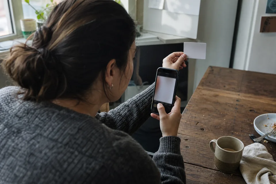 Hands holding a blank ID card next to a phone showing the camera frame